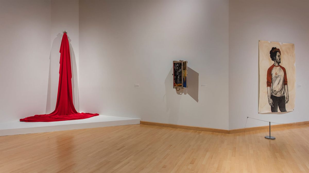 Installation view of paintings, sculpture, and red fabric flowing down wall