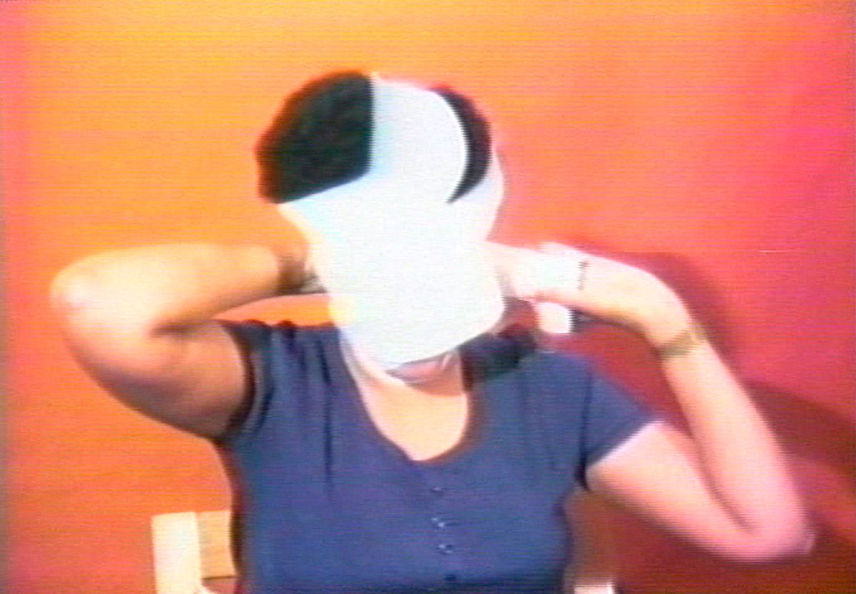 Still of the artist seated in a chair wrapping her head with white gauze