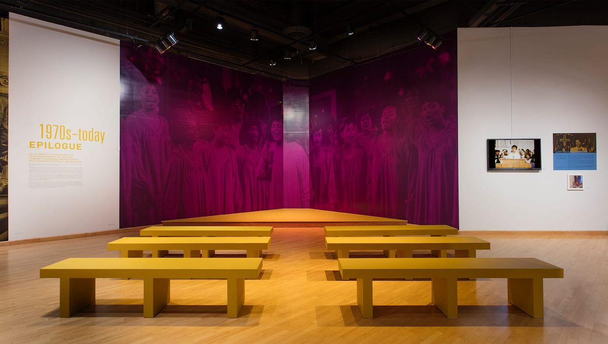 Installation view in back of seating arranged like church pews and facing large scale photo mural of a singing choir