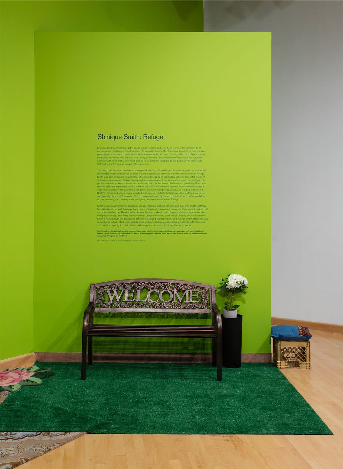 Against vivid green wall and astro turf a bench that reads, "welcome"