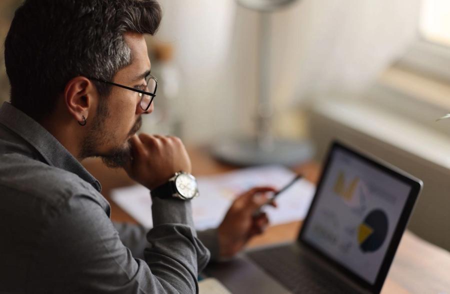 A focused man with glasses thoughtfully reviews financial pie charts and data on his laptop screen, optimizing his asset allocation across accounts.