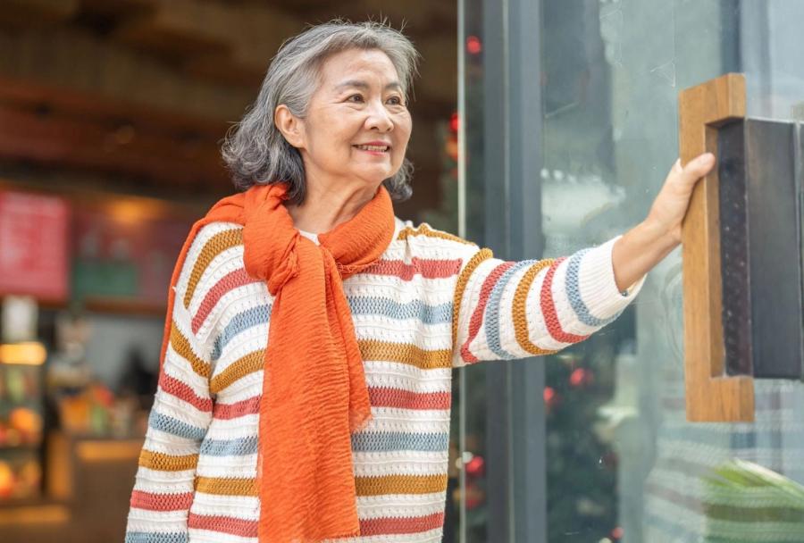 A smiling senior woman confidently enters a local shop, illustrating how smart budgeting and resourcefulness make living on social security alone a fulfilling and active chapter of life.