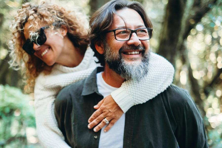 Man and woman carrying in piggyback and having fun together with love and friendship enjoying the outdoor leisure activity in nature park. Happiness and positive mindful attitude. Youthful old people