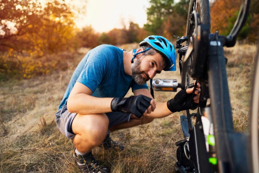 Middle-aged man in a bike helmet kneeling to adjust his mountain bike on a trail at sunset