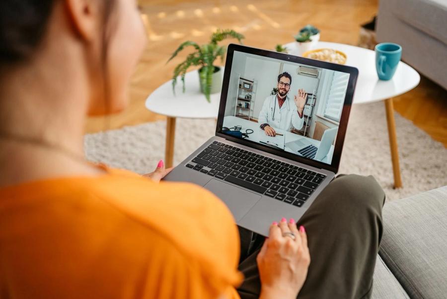 A woman sits on a sofa during a video appointment with a doctor on her laptop, representing the routine medical expenses that make up the average cost of healthcare in retirement.