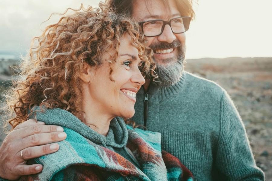 A smiling mature couple wearing cozy knit sweaters enjoying a scenic outdoor vista at sunset.