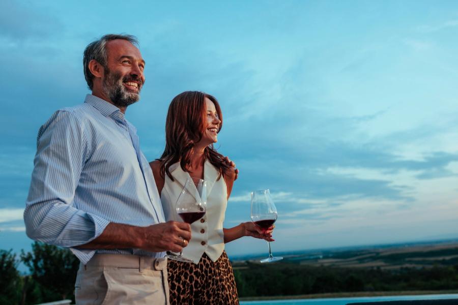Smiling couple sharing red wine at dusk, a picture of retirement for couples who talk about money and plan together
