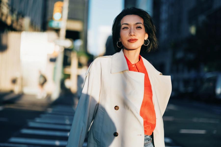A stylish Asian-American woman walks confidently along a city street, embodying the self-assurance of knowing she is on track for retirement.
