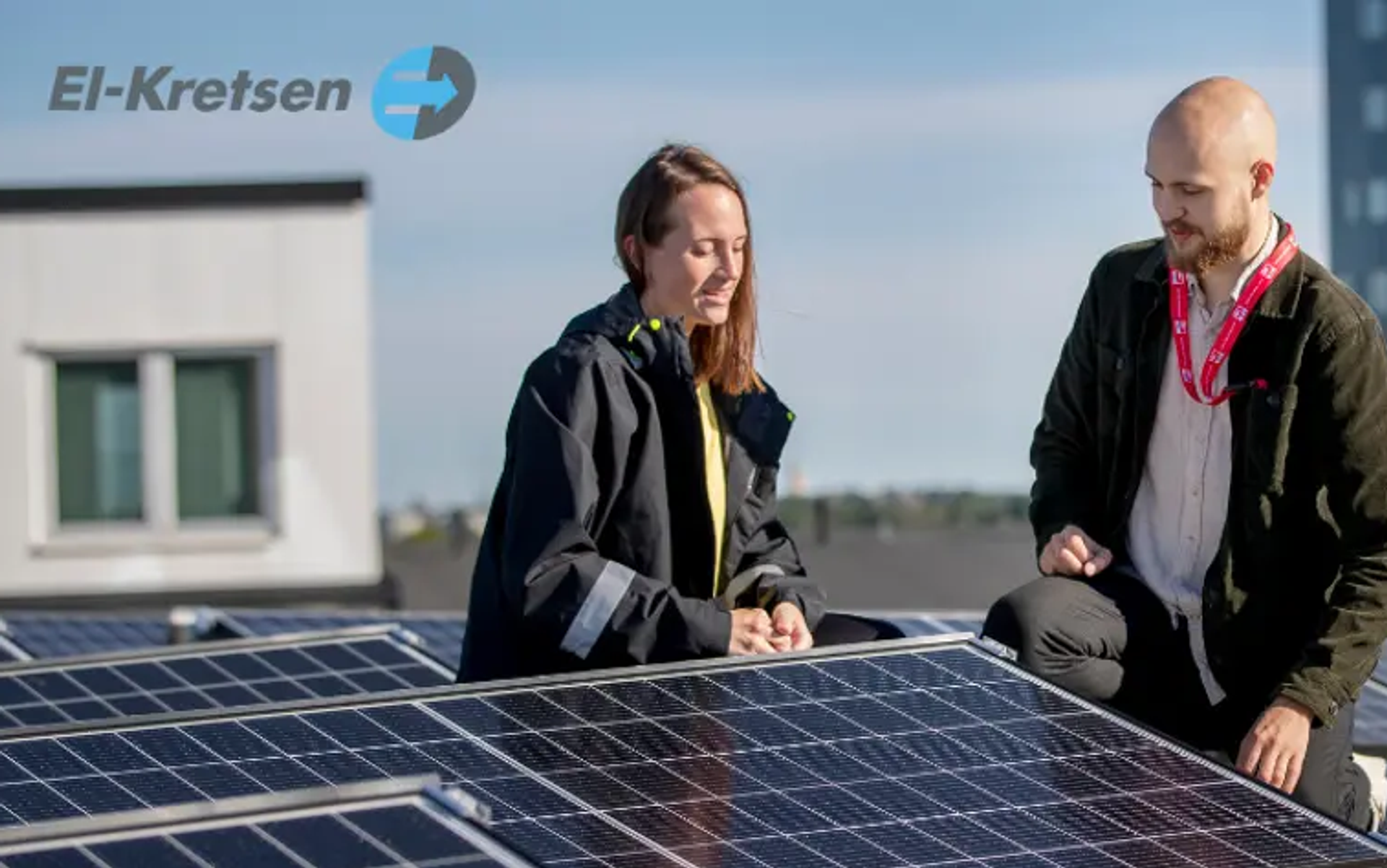 Två medarbetare från IBC SOLAR/Solkompaniet står på knä intill monterade solpaneler, på ett platt tak.