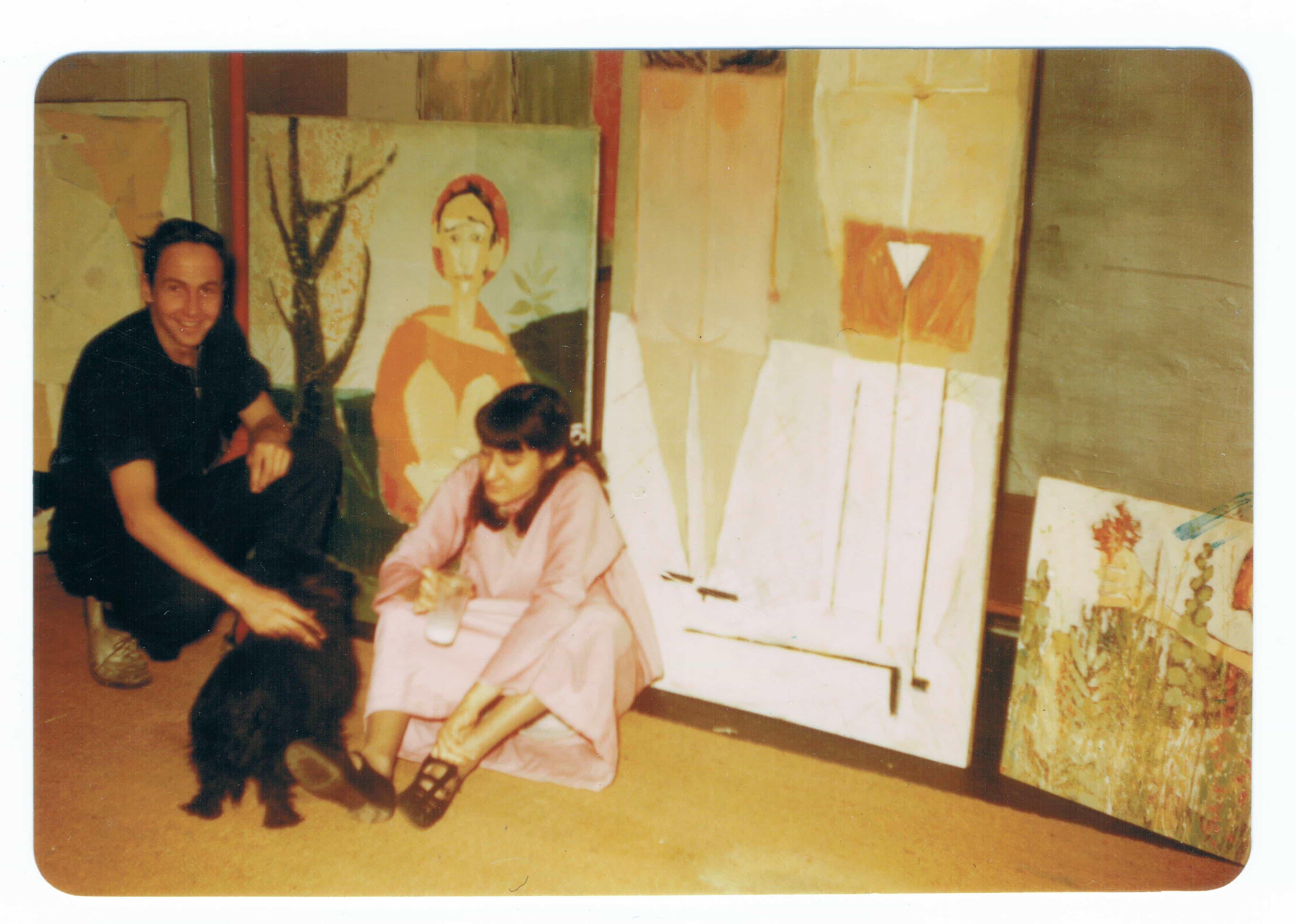An artist and his wife are posed in front of several abstract paintings in a studio setting.