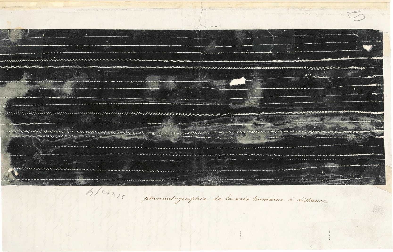 A vintage photograph featuring a long, dark strip with vertical lines and some faded areas, mounted on a paper with handwritten notes along the side.