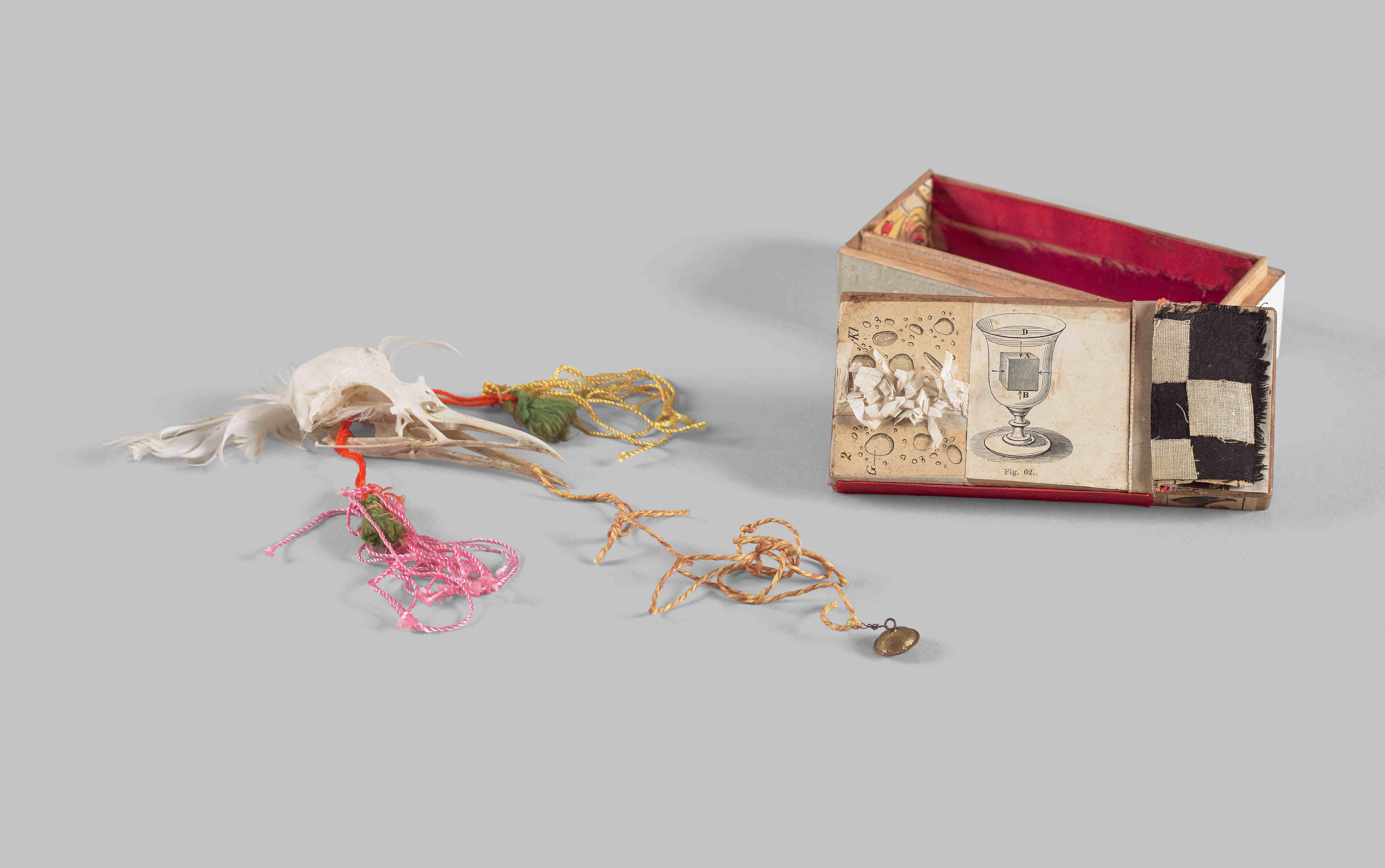 A small, decorative box with a painted design featuring a glass and checkered pattern, accompanied by colorful threads and tassels.