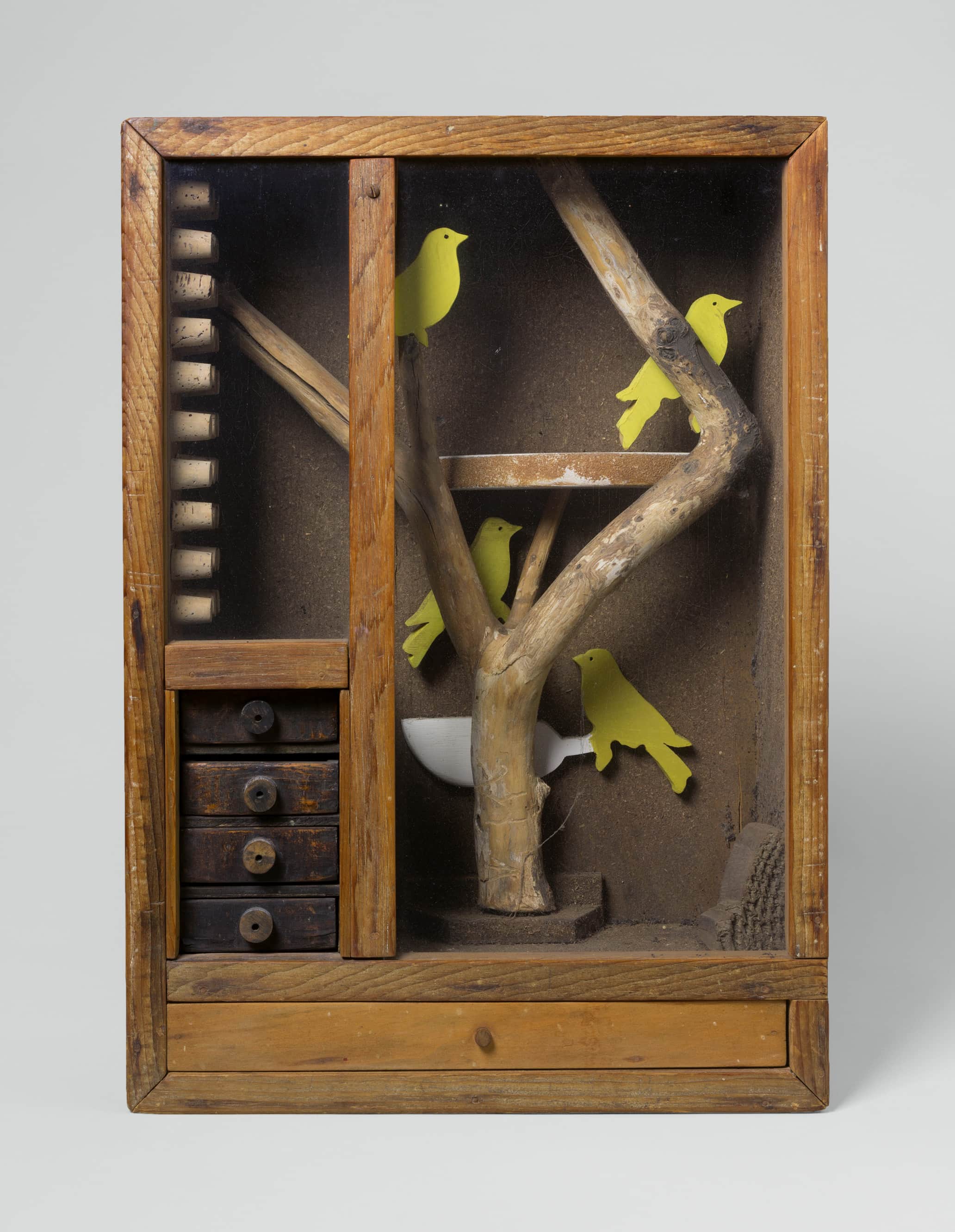 A wooden box depicts a miniature scene of three yellow birds perched on a branch within a small, earthy landscape.