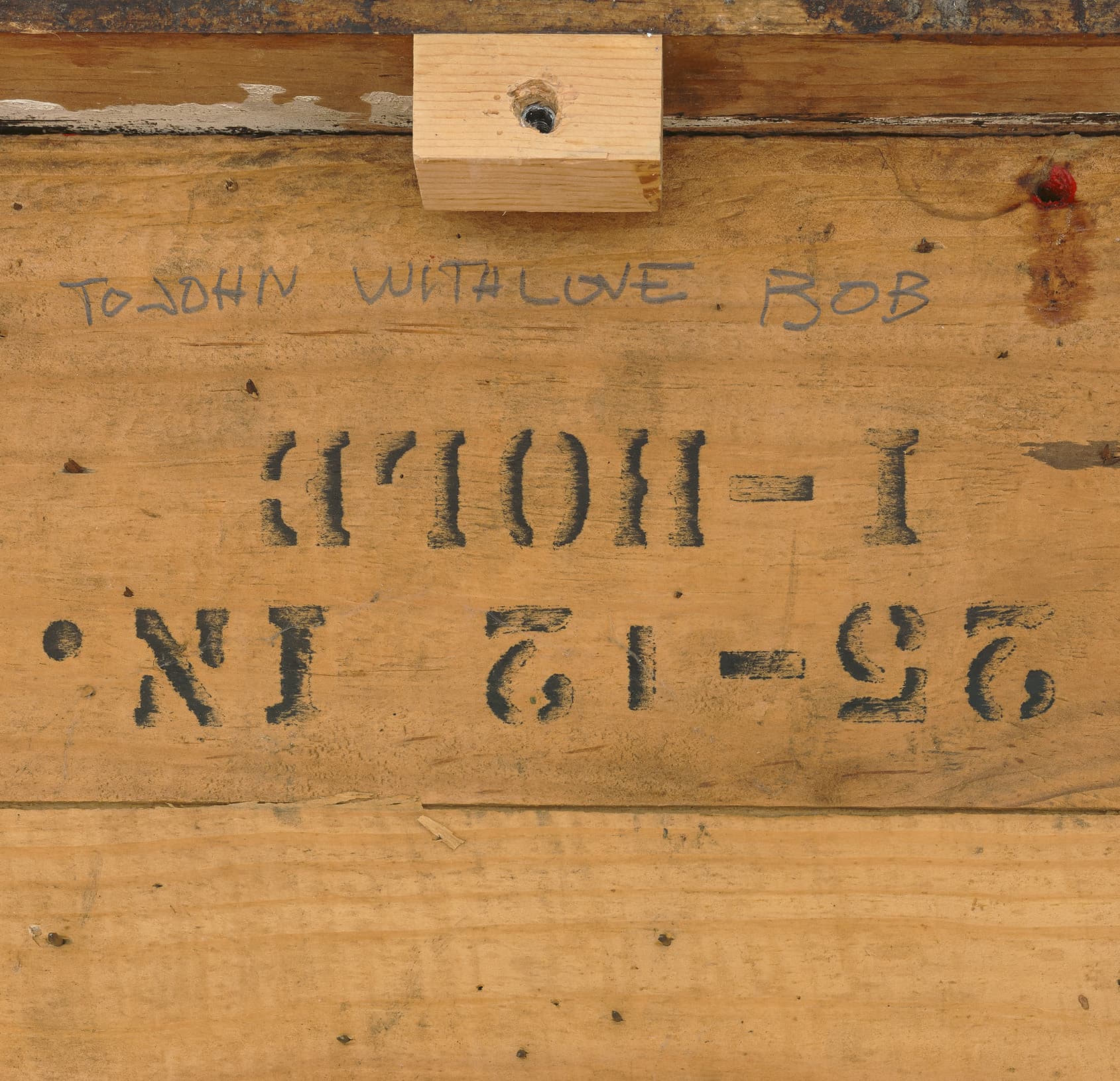 The image shows the back of a wooden crate with various stamps and markings, including numbers and text, and wooden supports at the corners.