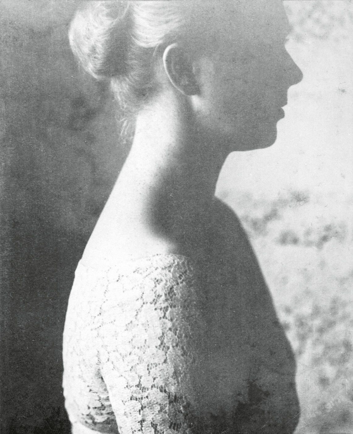 A vintage black and white photograph depicts a woman's profile, partially obscured by shadow and wearing a lace top.