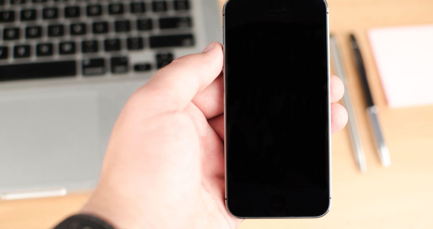 A hand holds a smartphone beside a laptop.