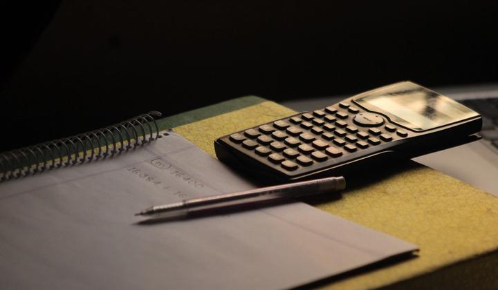 A calculator and pen rest on an open notebook.