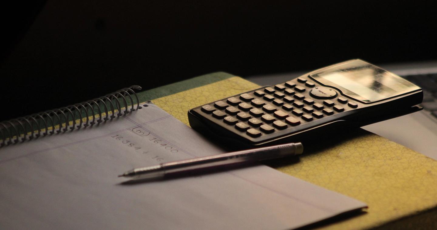 A calculator and pen rest on an open notebook.
