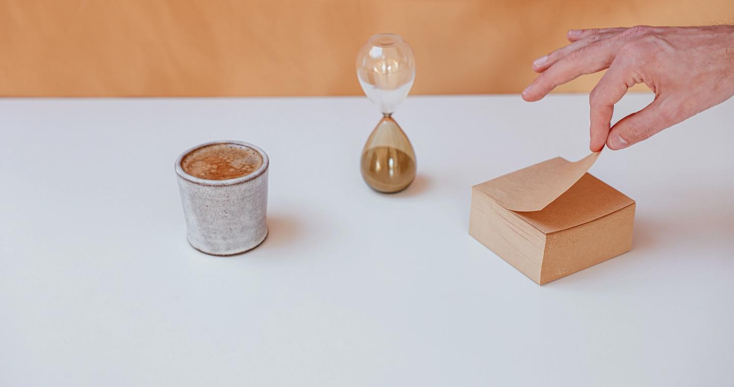 An hourglass, coffee cup and notepad on a white desk.