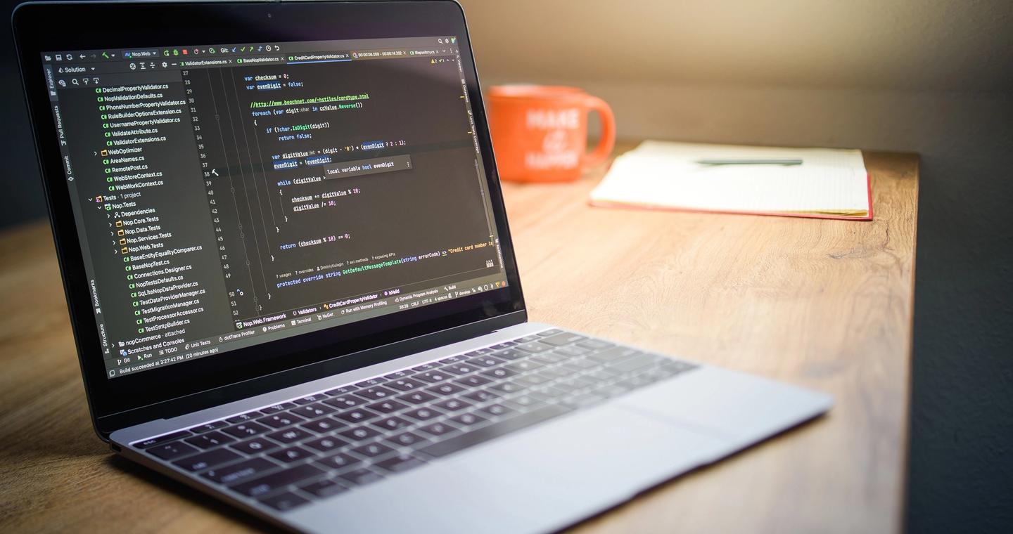 A laptop displaying code sits beside a notebook and a mug.