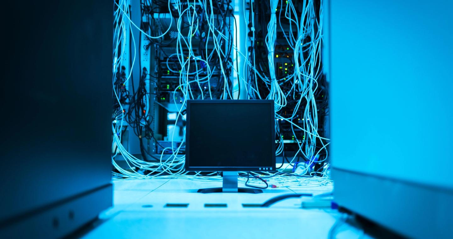A monitor stands beside network cables in a server room.