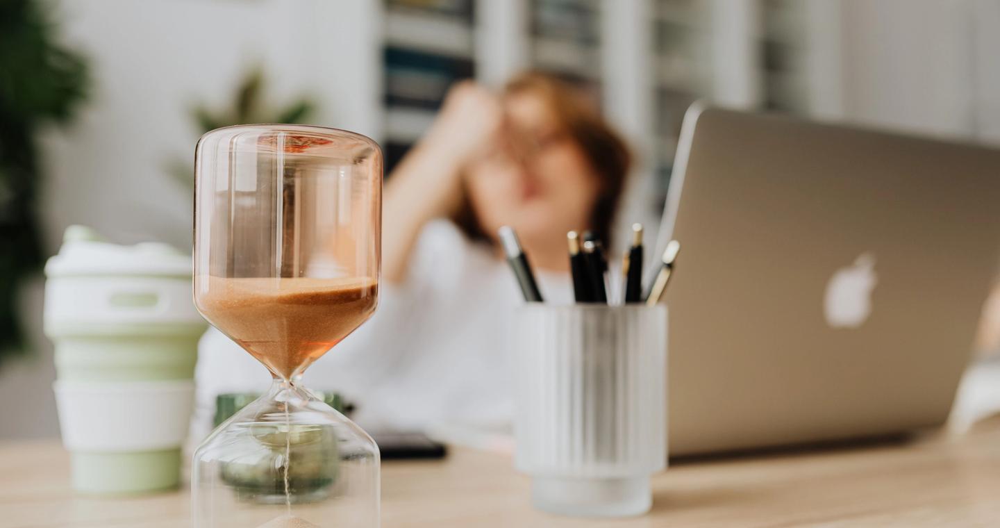An hourglass beside a laptop on a work desk.