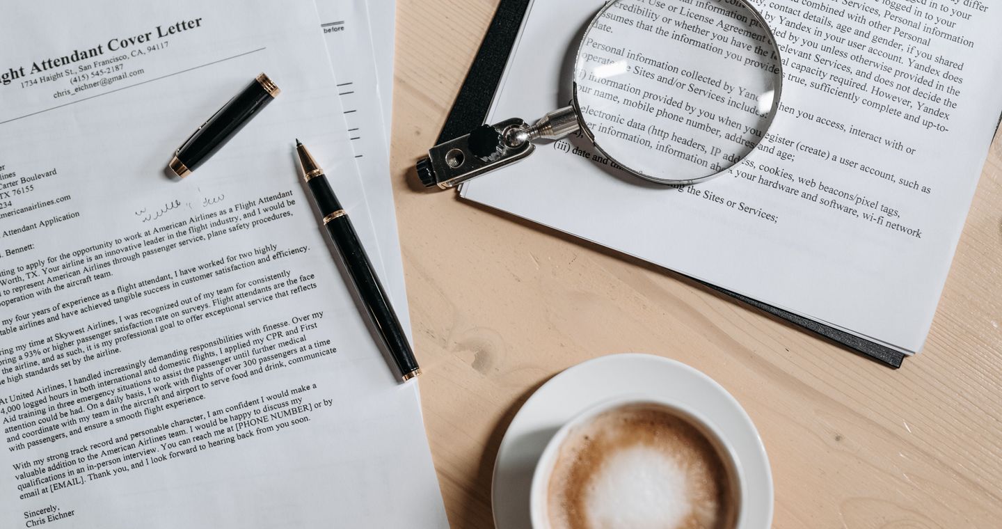 A magnifying glass, coffee and papers on a wooden desk.