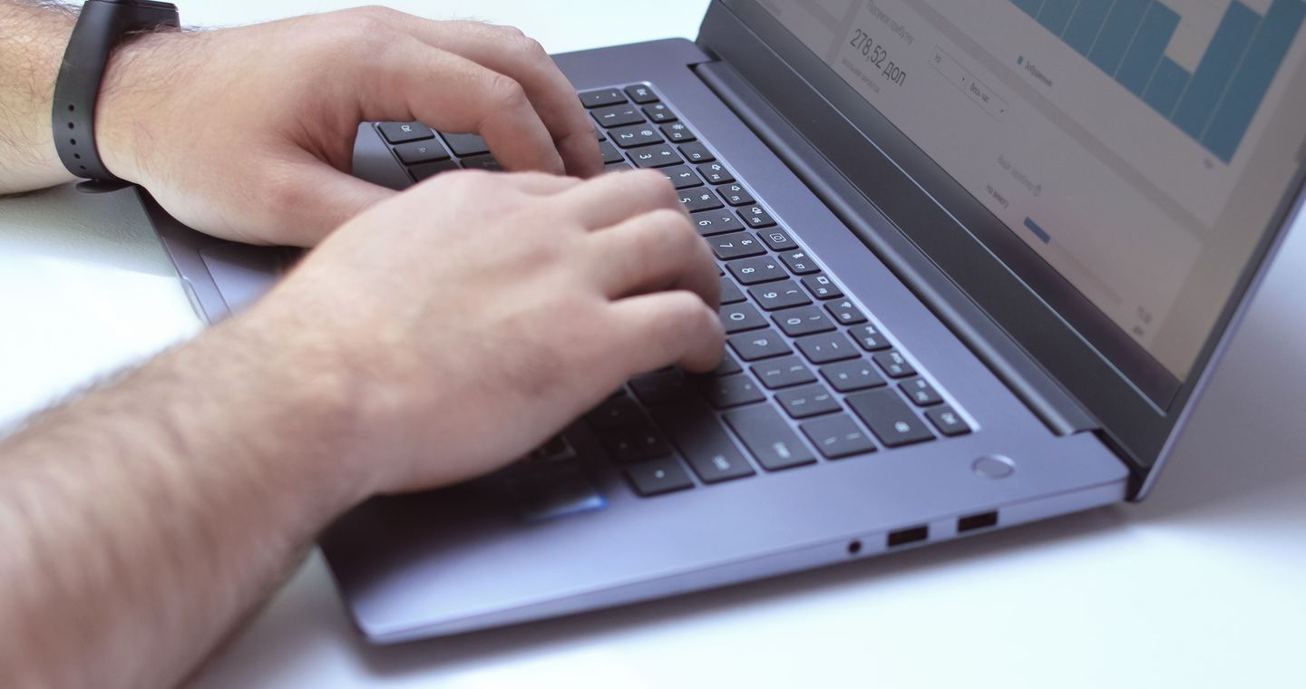 Hands typing on a laptop with charts on its screen.