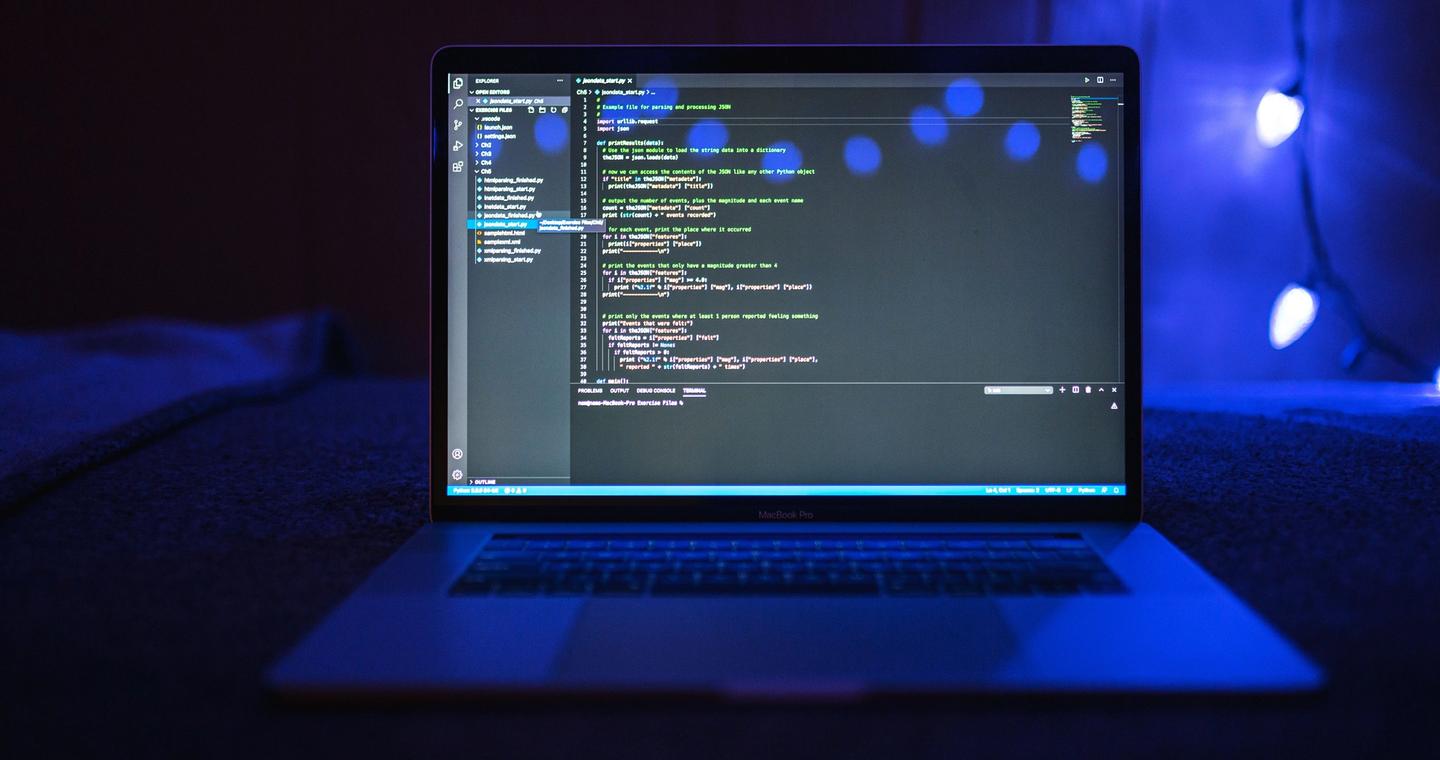A laptop screen displaying source code in a dim workspace.