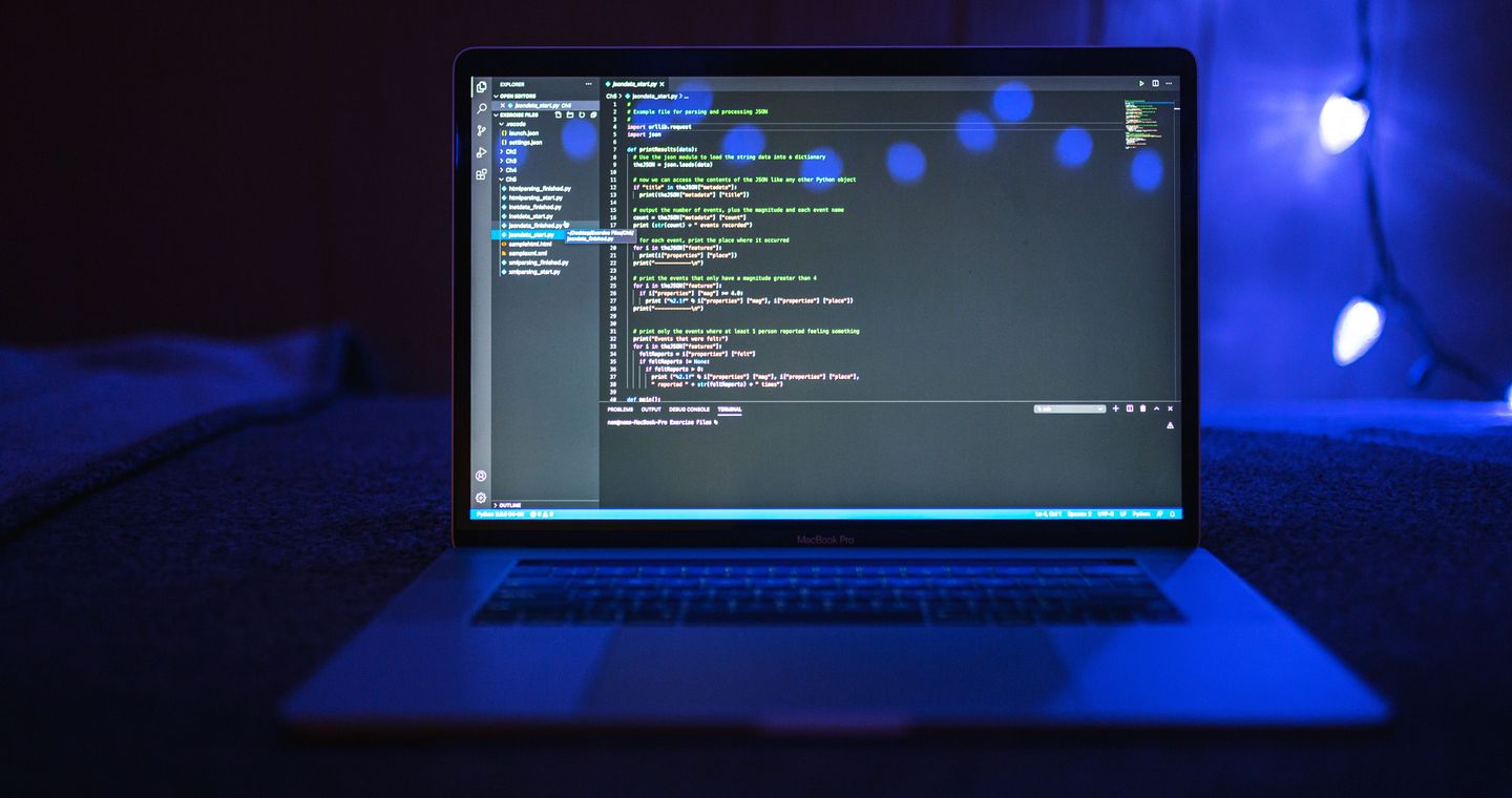 A laptop screen displaying source code in a dim workspace.