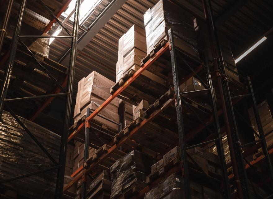 Cardboard boxes stand on tall shelves inside a warehouse.