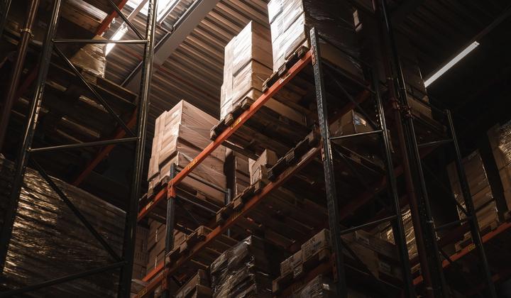 Cardboard boxes stand on tall shelves inside a warehouse.