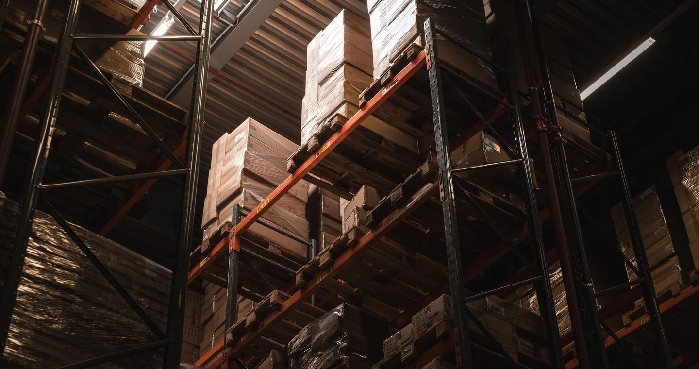 Cardboard boxes stand on tall shelves inside a warehouse.