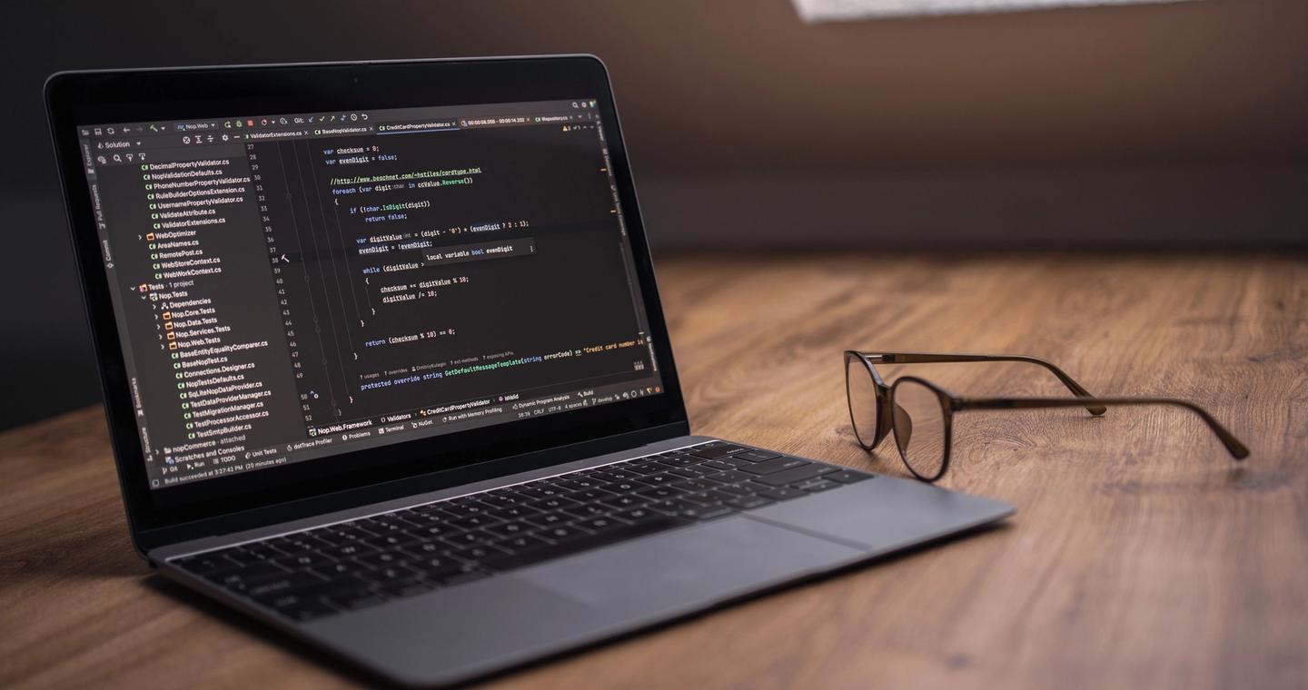 A laptop with a code editor and eyeglasses on a wooden desk.