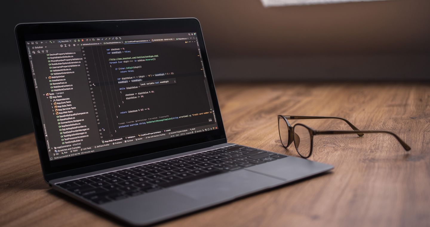 A laptop with a code editor and eyeglasses on a wooden desk.