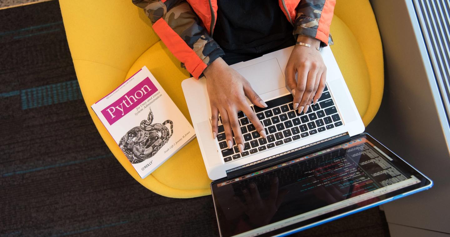A developer using a laptop beside a Python programming book.