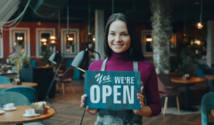 A woman holds an open sign inside a cafe.
