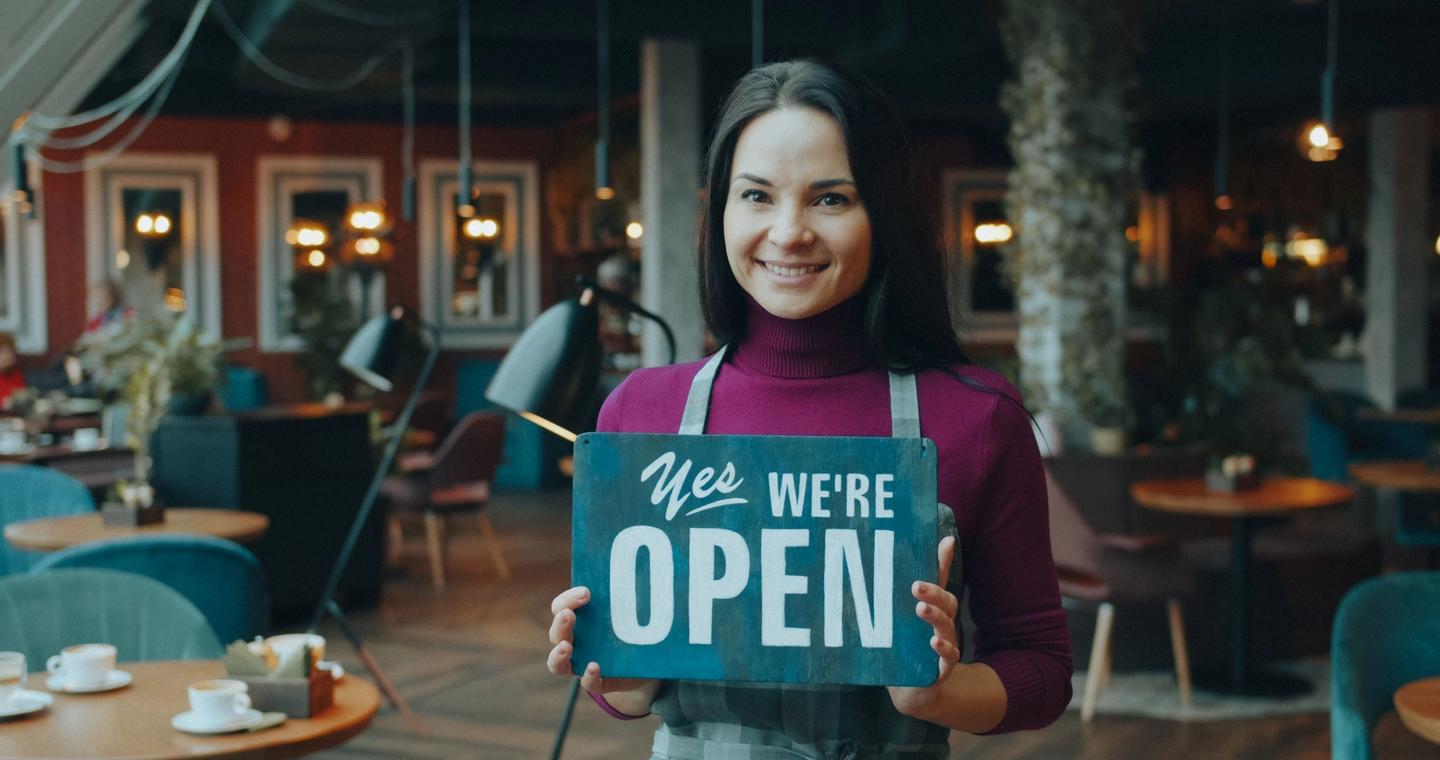 A woman holds an open sign inside a cafe.