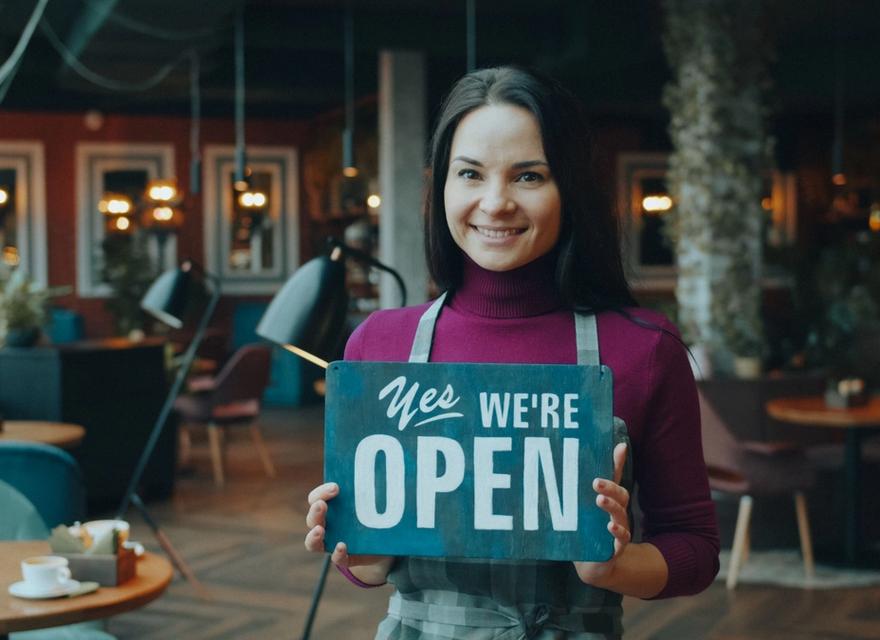 A woman holds an open sign inside a cafe.