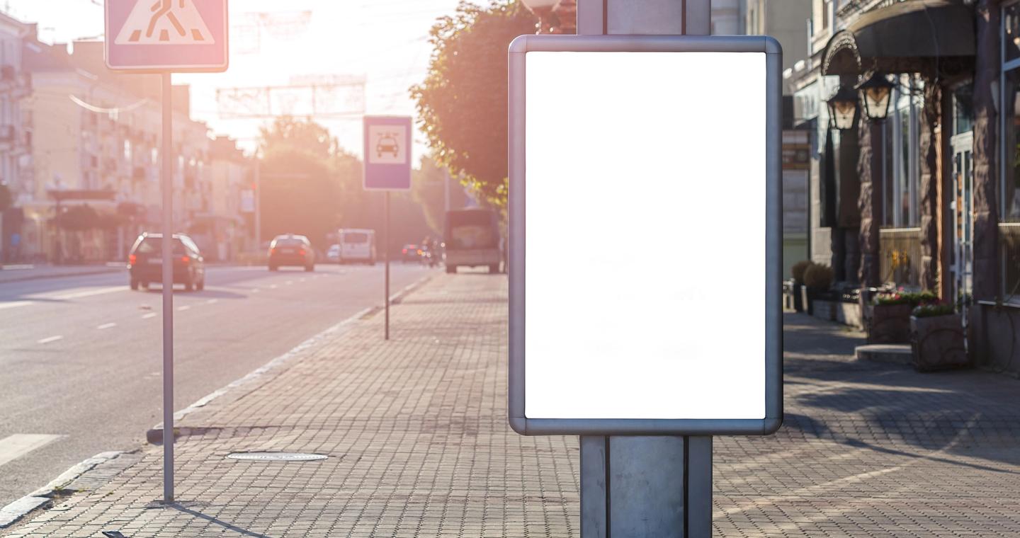 An empty advertising display beside a sunny city street.