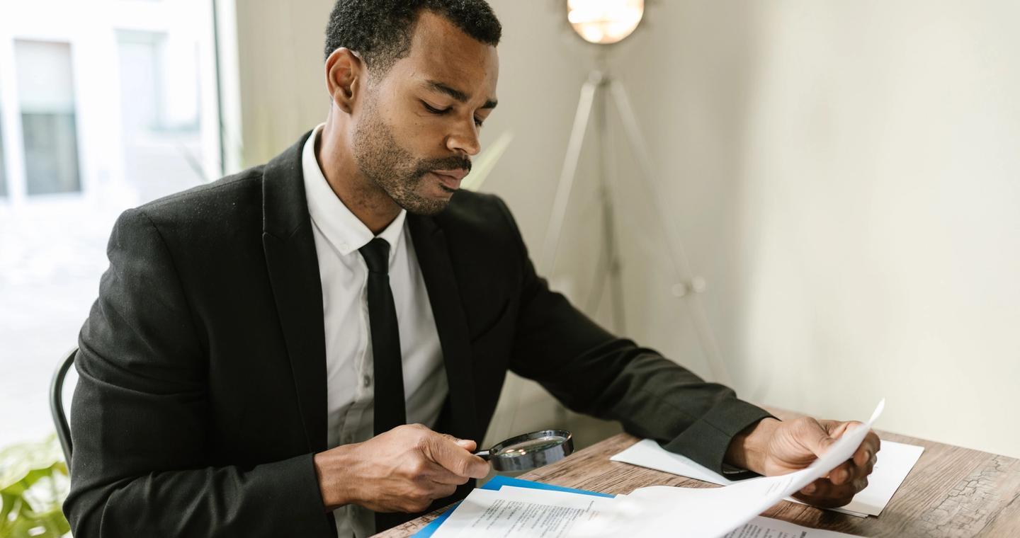 A person examining papers with a magnifying glass.