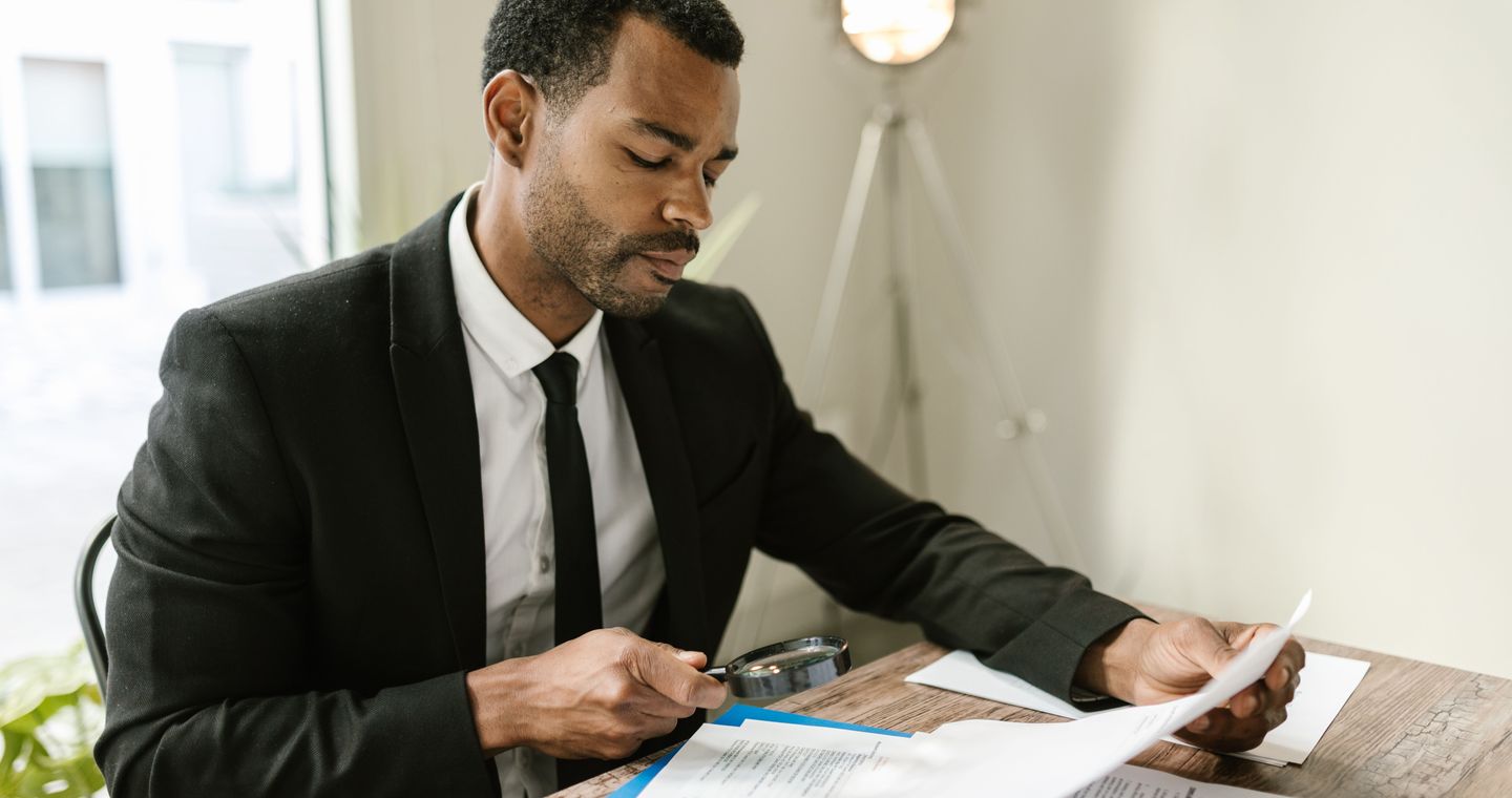 A person examining papers with a magnifying glass.