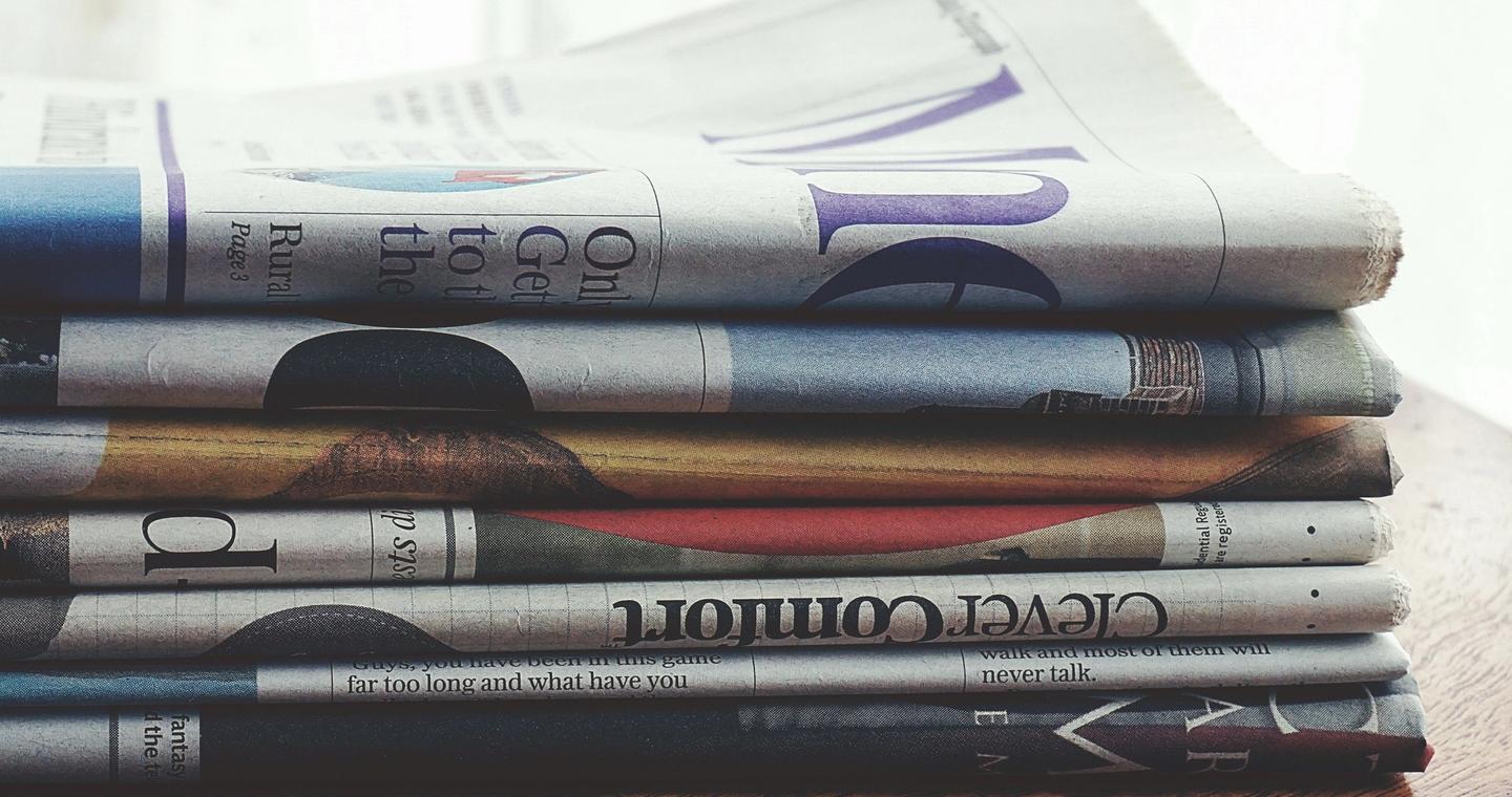 Folded newspapers stacked on a wooden table.