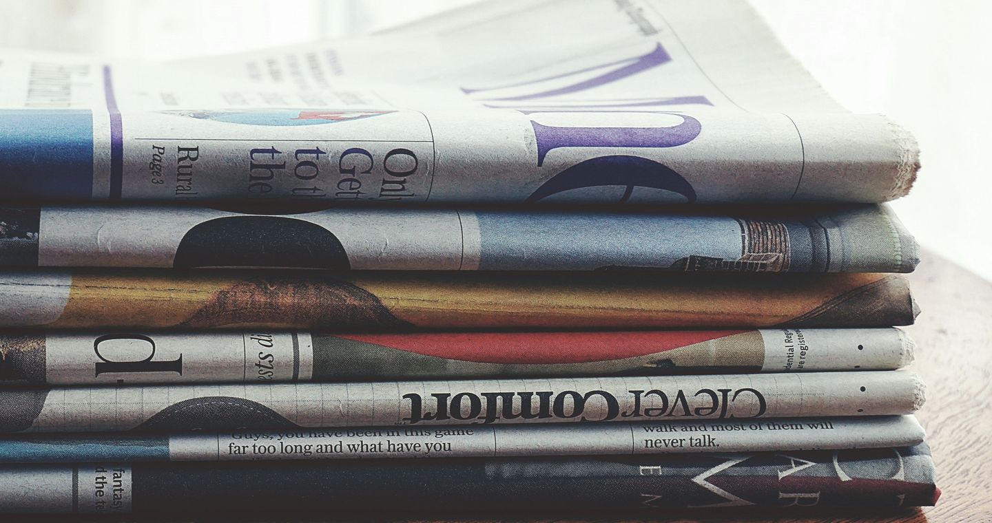 Folded newspapers stacked on a wooden table.