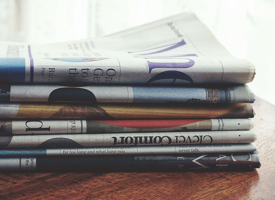 Folded newspapers stacked on a wooden table.