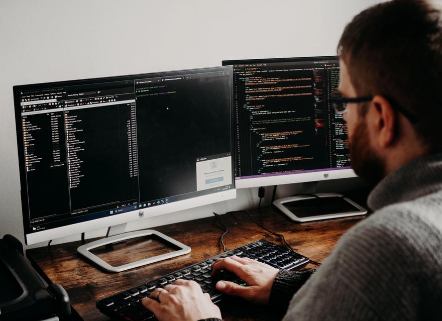 A person types at a desk with two monitors.