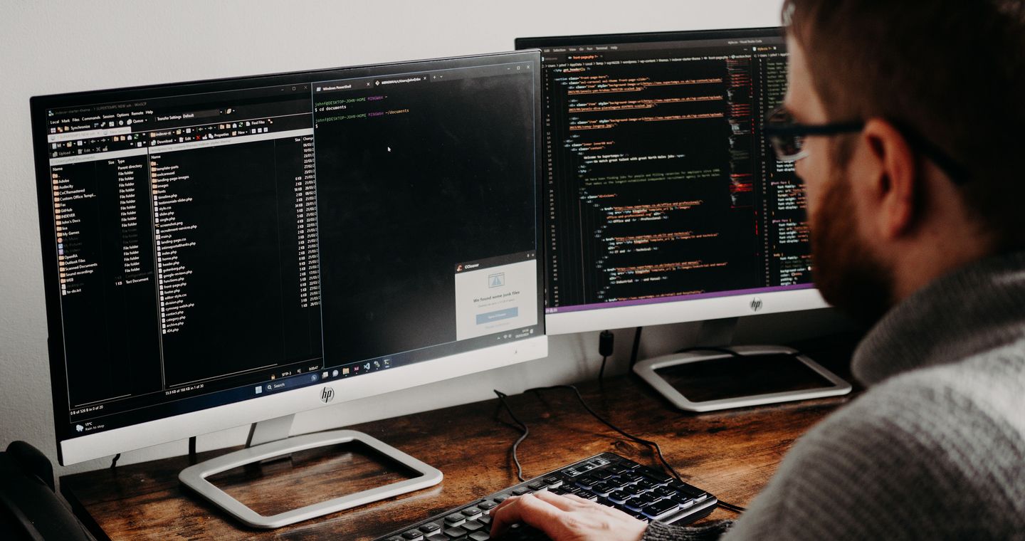 A person types at a desk with two monitors.