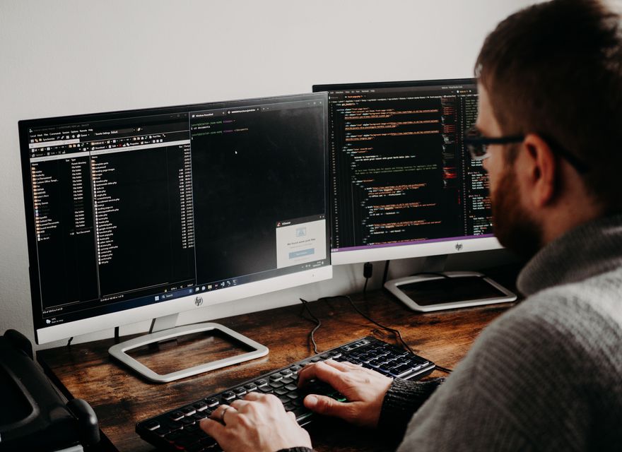 A person types at a desk with two monitors.