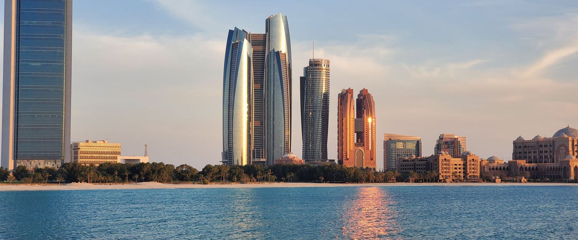 Abu Dhabi skyline of modern towers reflected in the sea at sunset