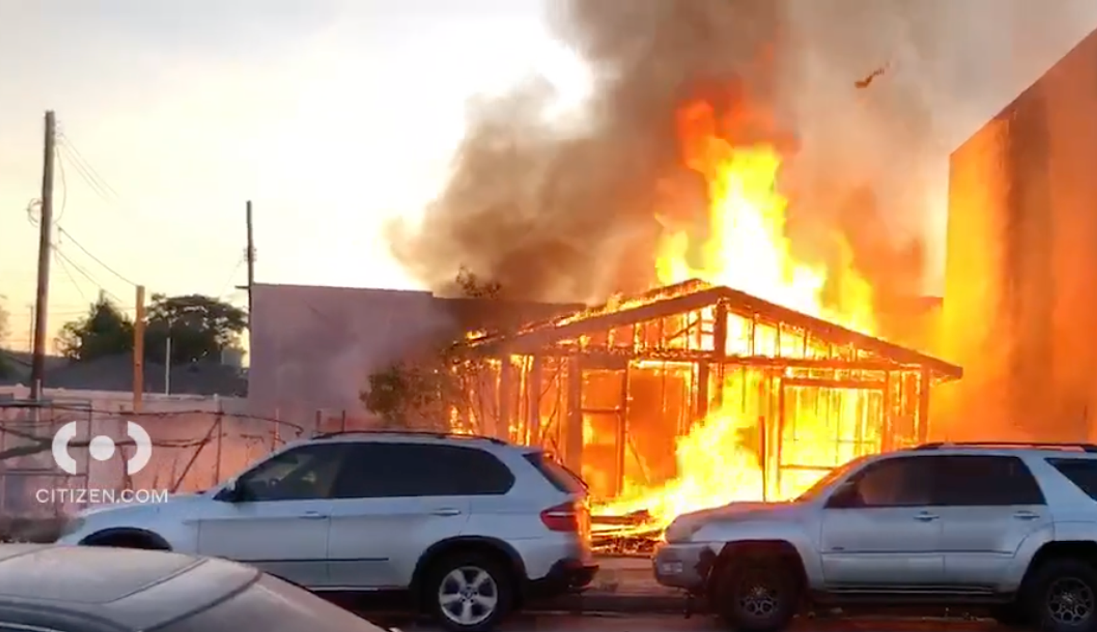 6743 Irvine Avenue, burned down to the studs and actively on fire, behind two silver SUVs.